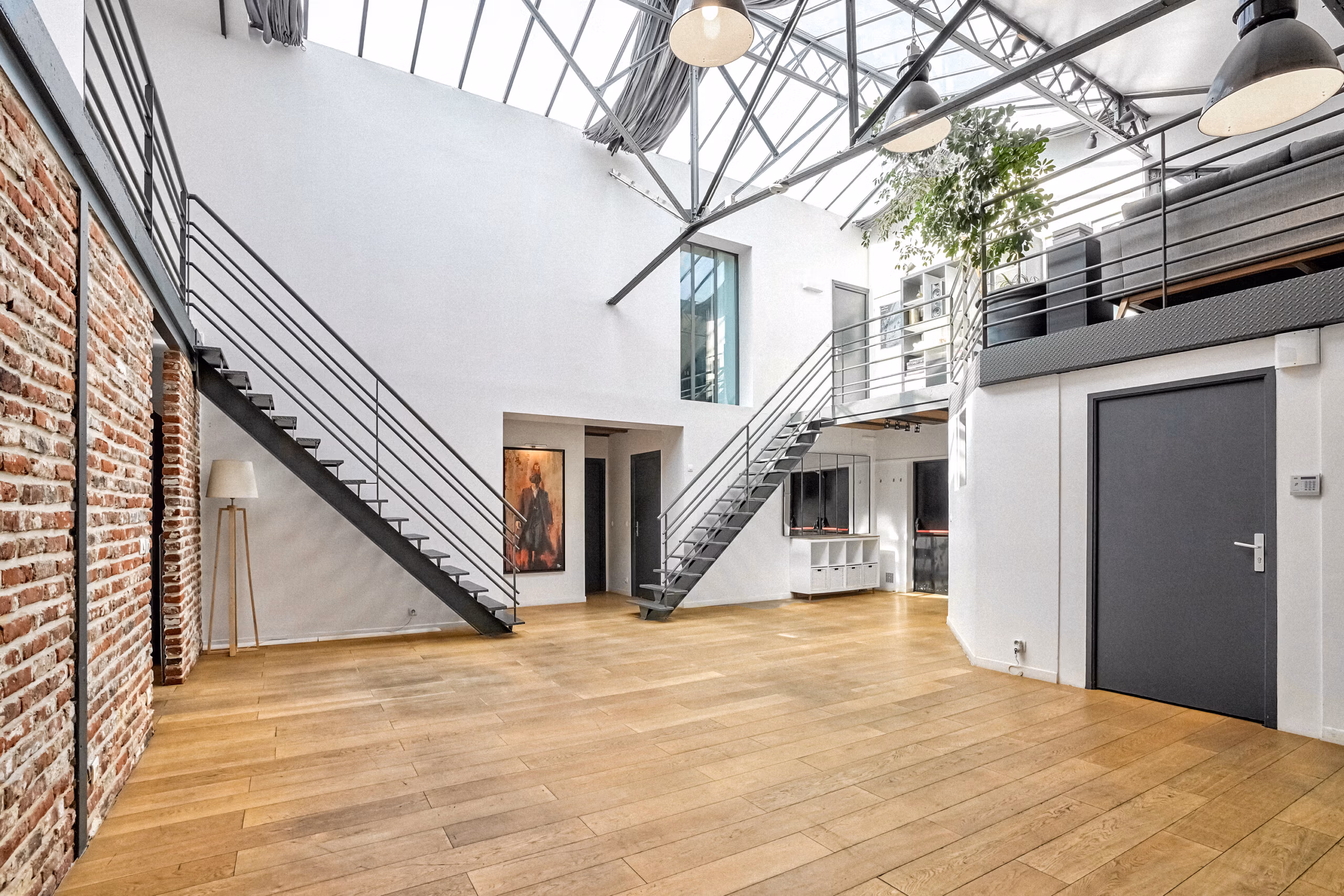Espace central du duplex avec verrière cathédrale, double escalier design, murs briques apparentes et parquet bois pour productions audiovisuelles et shootings photo