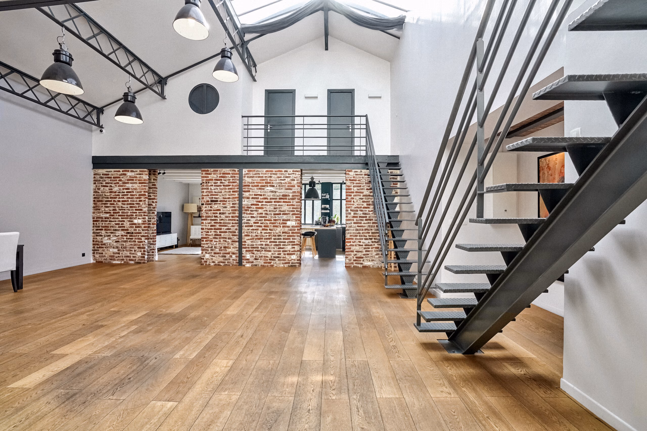 Studio avec colonnes de briques apparentes d'époque, mezzanine accessible, luminaires industriels suspendus et parquet massif pour tournages clips et films publicitaires