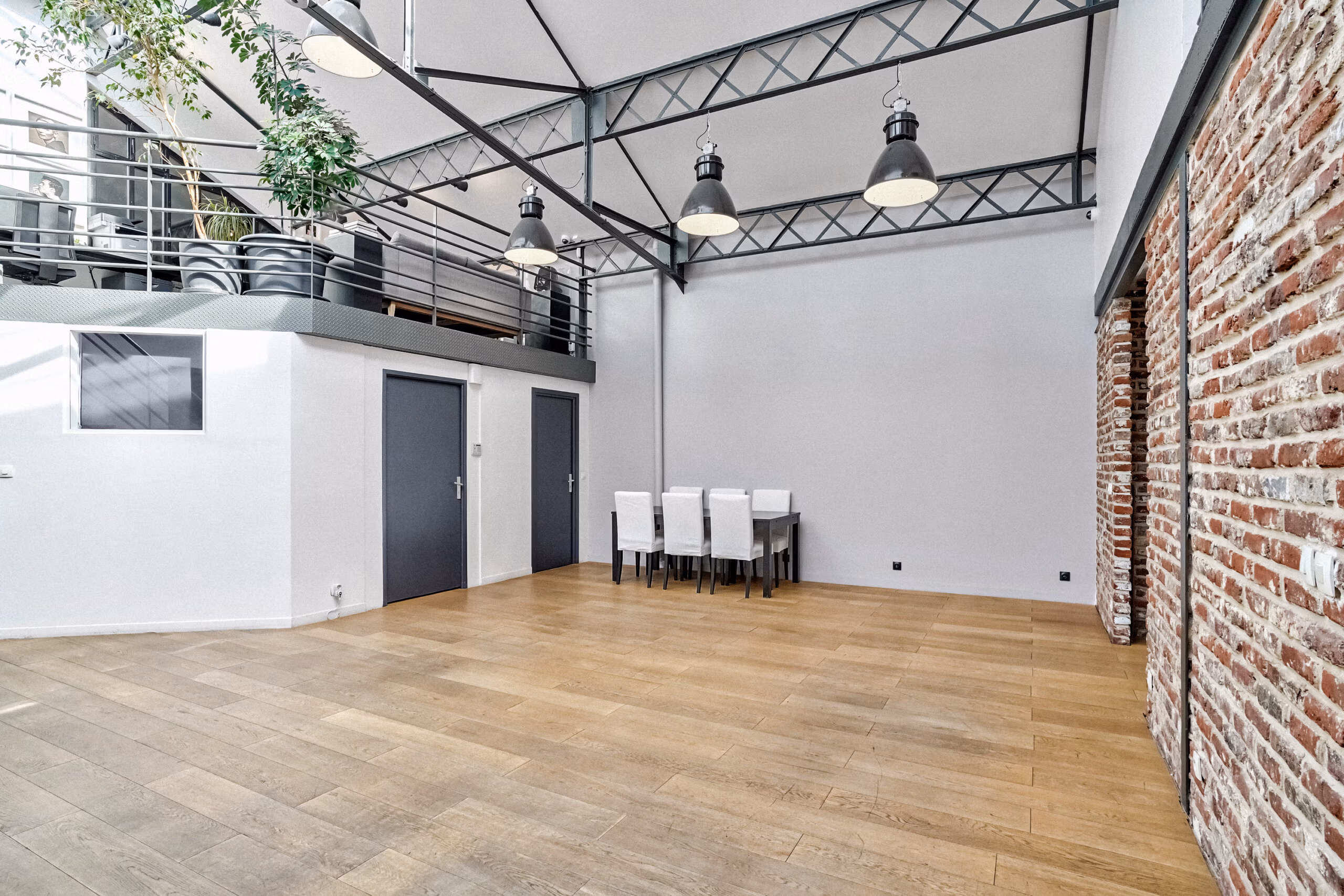 Grand patio avec mezzanine ouverte, luminaires suspendus industriels, parquet bois et grandes hauteurs pour événements professionnels et showrooms