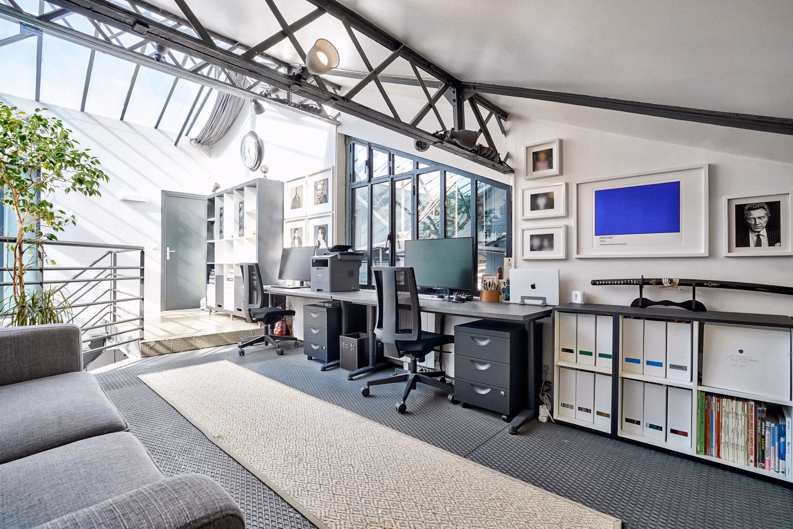 Bureau en mezzanine sous poutres métalliques Eiffel avec galerie de photos d'art encadrées, bibliothèque rangement et verrière pour réunions créatives et séminaires production