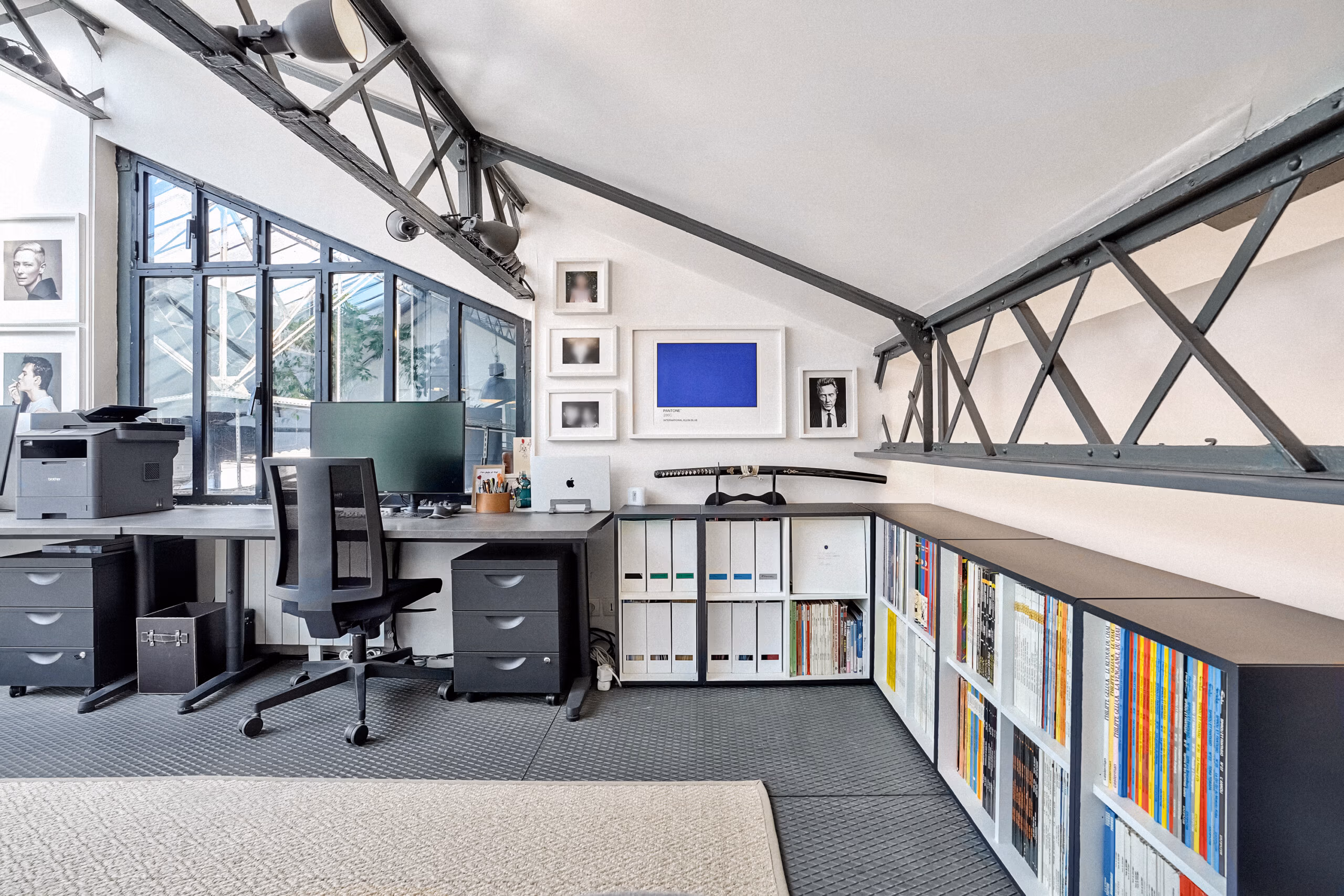 Espace de travail mezzanine avec collection de portraits photographiques encadrés, bibliothèque colorée et structure métallique apparente pour interviews et contenus culturels