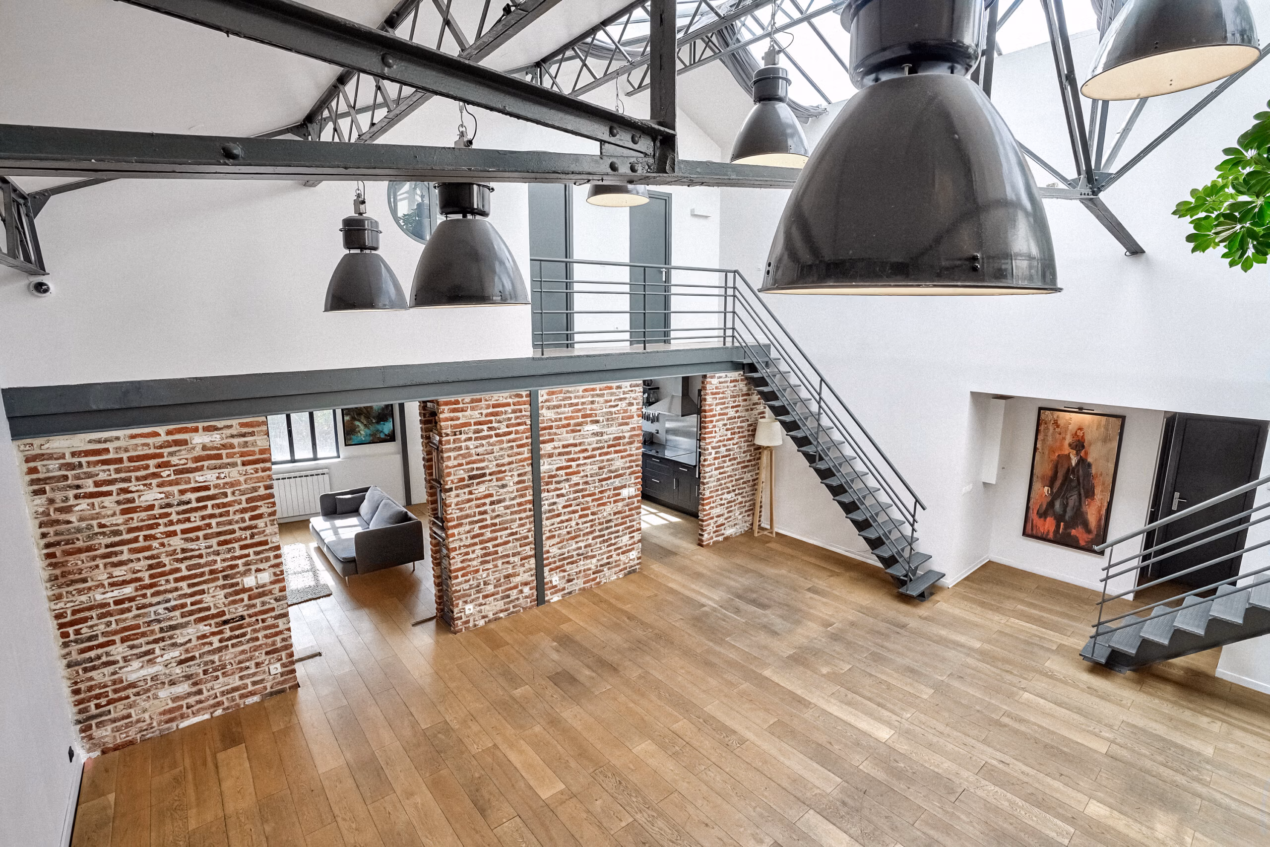 Vue plongée depuis mezzanine sur le duplex avec luminaires industriels XXL suspendus, colonnes de briques structurantes et double hauteur pour tournages TV et clips en top shoot