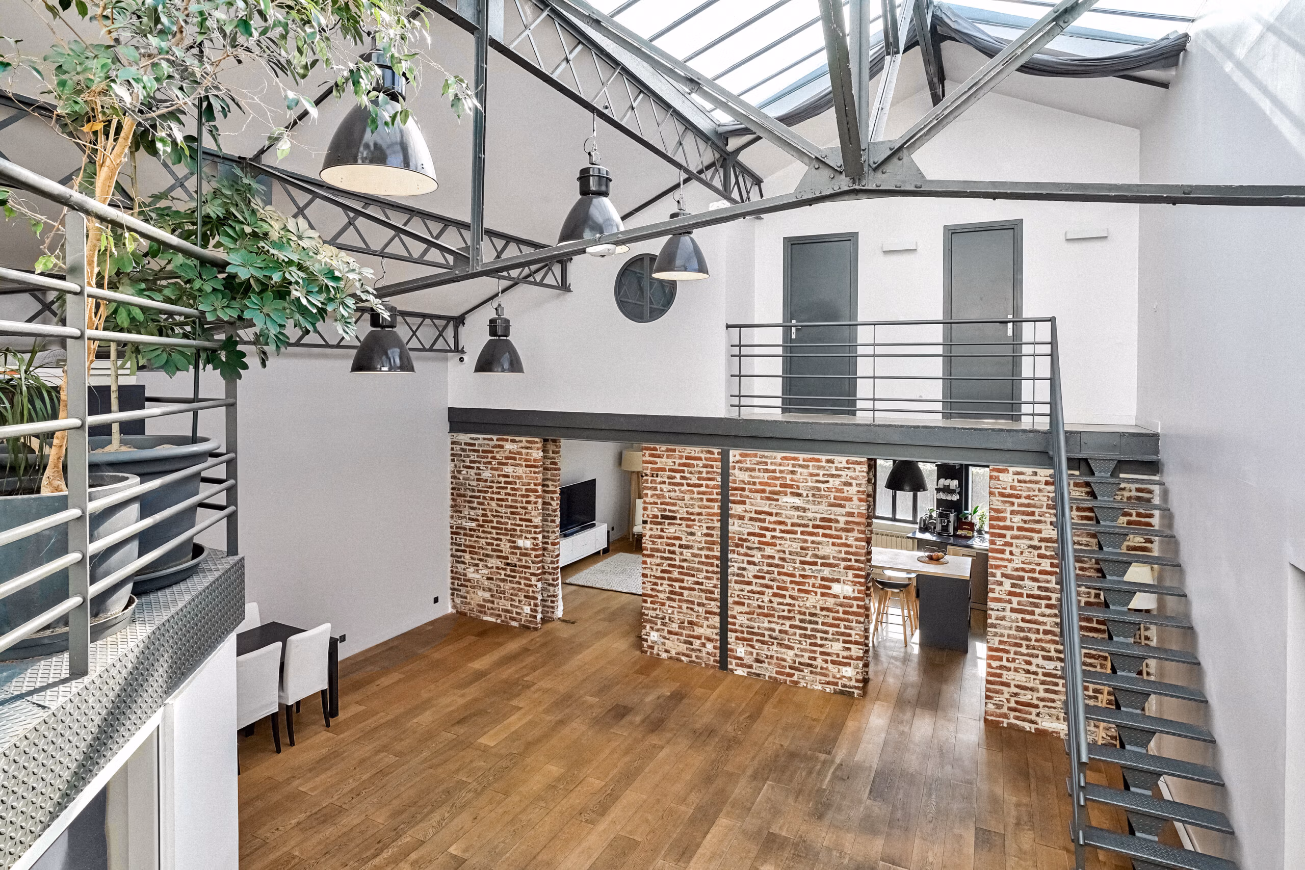 Vue top shoot du salon-cuisine avec colonnes de briques apparentes, verrière cathédrale, végétation XXL et mezzanine ouverte pour productions web et shootings architecture