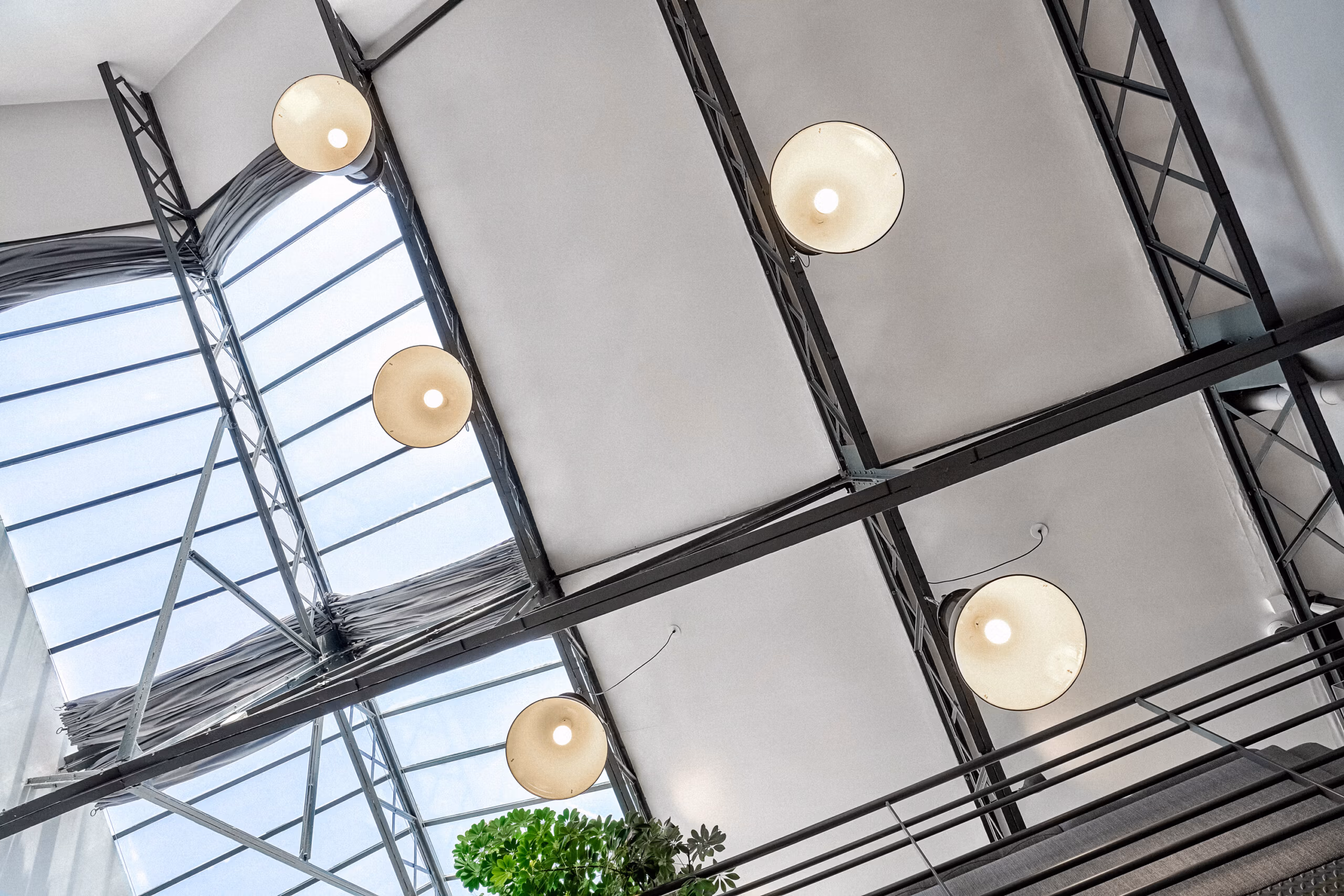 Vue plongée sur la verrière cathédrale avec luminaires industriels suspendus, structure métallique Eiffel et végétation intérieure