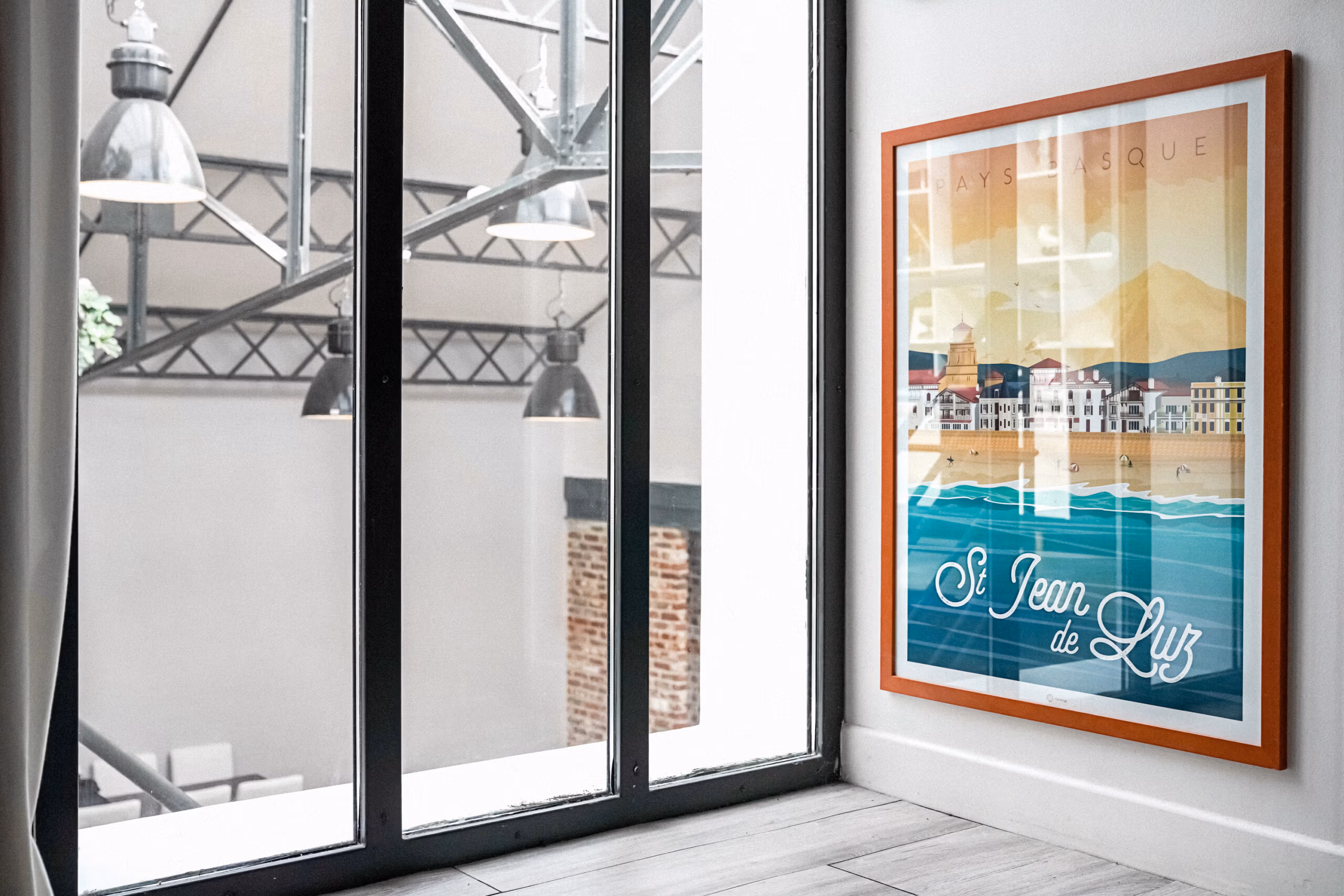 Affiche vintage encadrée devant baie vitrée type atelier avec vue sur structure métallique, ajoutant une touche décorative pour shootings lifestyle et contenus voyages