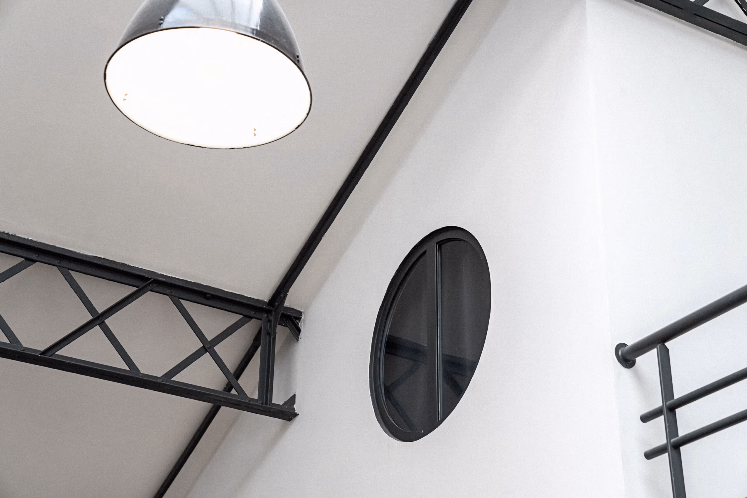 Hublot circulaire noir style naval avec luminaire industriel suspendu et poutres métalliques triangulées, détail architectural pour shootings design et contenus déco