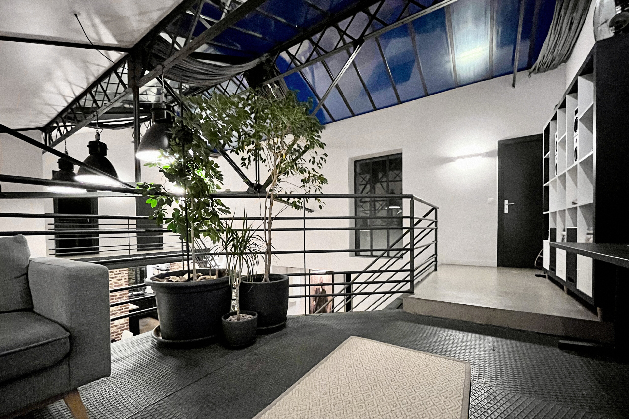 Ambiance nocturne mezzanine avec éclairage artificiel, verrière illuminée en bleu, végétation intérieure et garde-corps tubulaire pour tournages de nuit et contenus atmosphériques