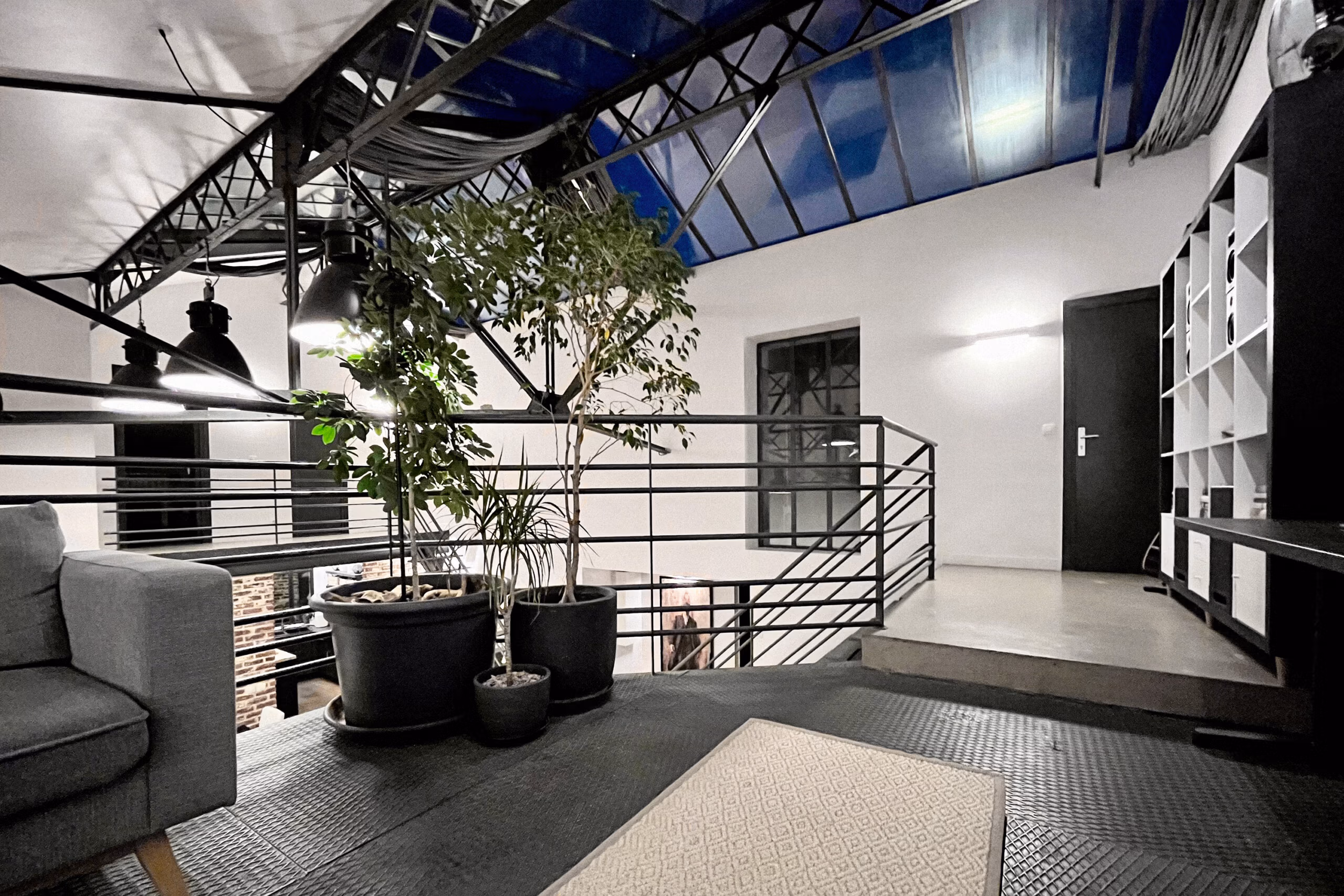 Ambiance nocturne mezzanine avec éclairage artificiel, verrière illuminée en bleu, végétation intérieure et garde-corps tubulaire pour tournages de nuit et contenus atmosphériques