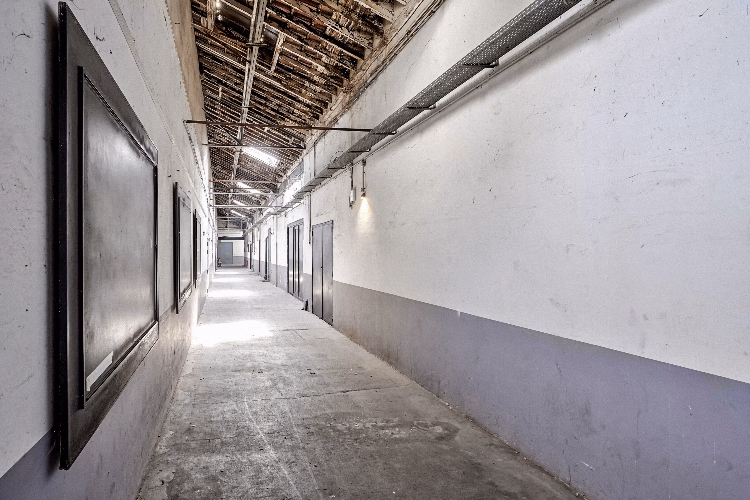 Couloir des anciens entrepôts SNCF avec béton brut, portes métalliques alignées et charpente bois visible pour tournages et shooting mode dans une atmosphère industrielle