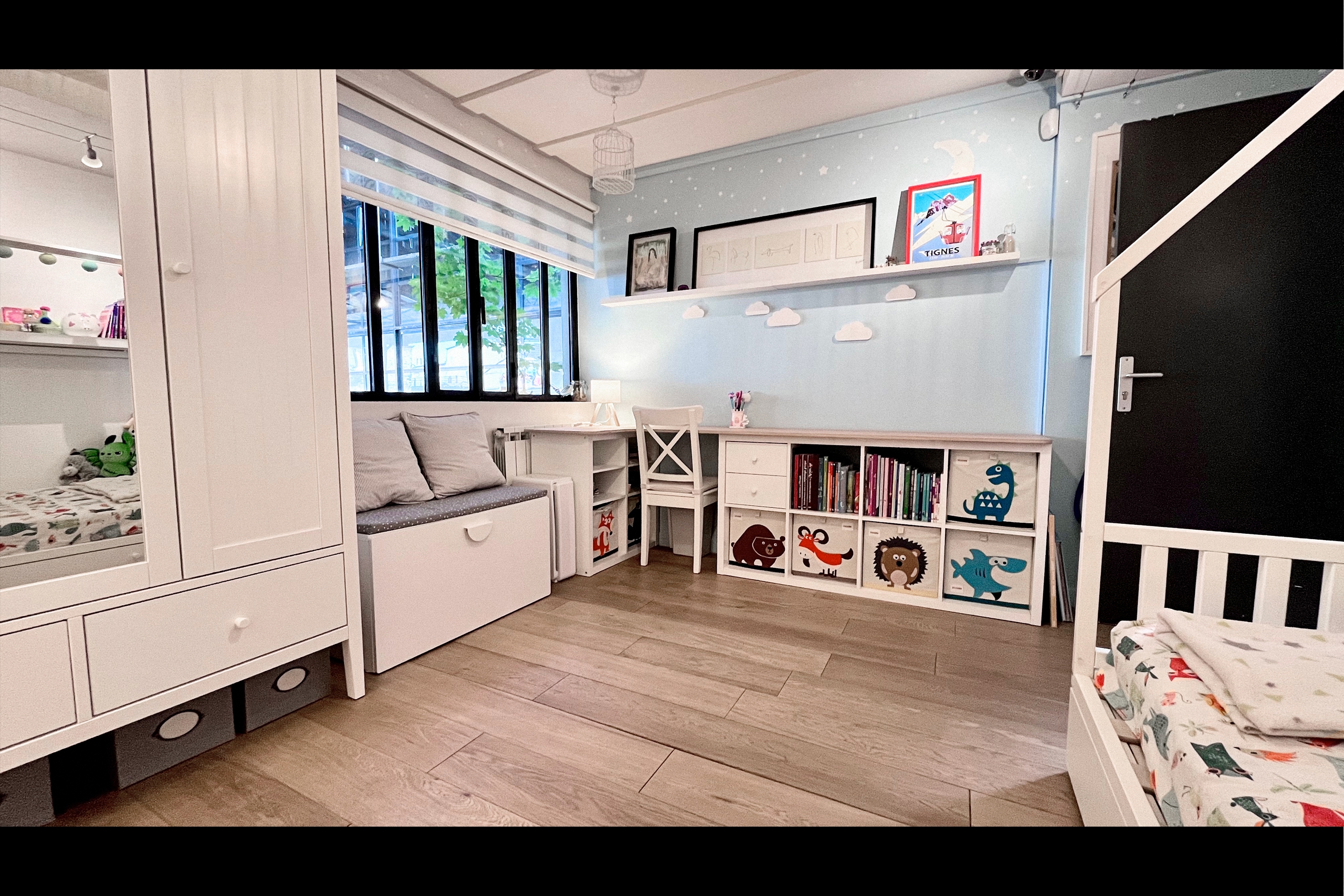 Coin bureau chambre enfant sous fenêtre atelier acier noir, mur bleu ciel étoilé, nuages muraux et cubes de rangement illustrés pour shootings puériculture et publicité jouets