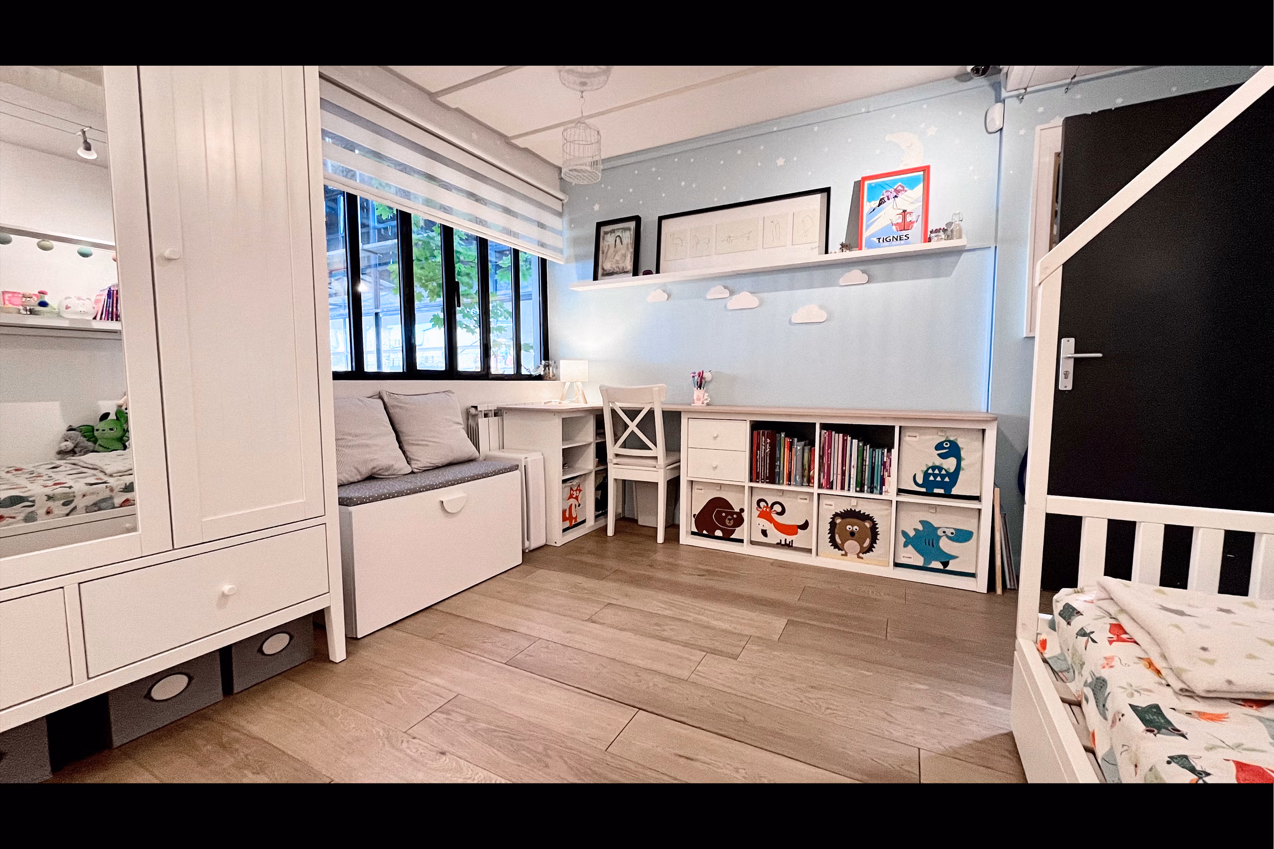 Coin bureau chambre enfant sous fenêtre atelier acier noir, mur bleu ciel étoilé, nuages muraux et cubes de rangement illustrés pour shootings puériculture et publicité jouets